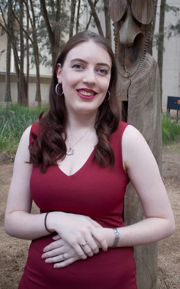 [Image description: A photo of Emma at a friend's wedding back in 2019. Her brown hair is curled and she wears a red sleeveless dress. End description. ]